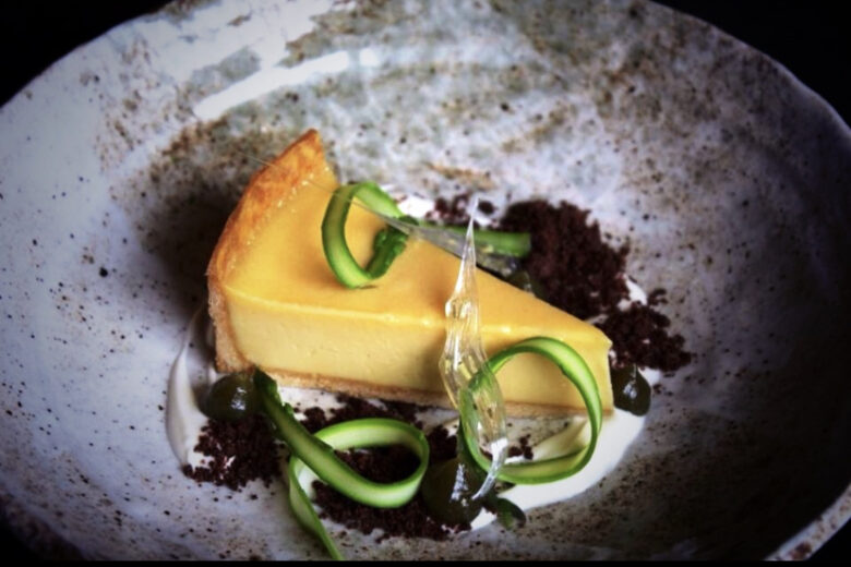 A sunshine yellow custard tart slice with ribbons of asparagus in a charcoal-grey bowl
