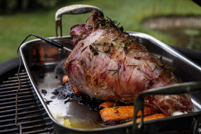 A lamb joint sat on a bed of carrots in a ProWare stainless steel roasting pan, atop a barbecue