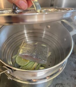 Stainless Steel Tri-Ply Steamer with a piece of fish and lemongrass inside and the lid being lifted off