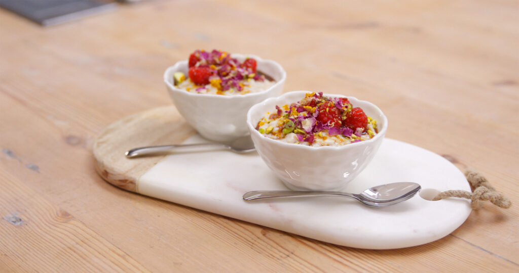 A pair of bowls with spiced rice pudding served topped with raspberries and dried rose petals and pistachios